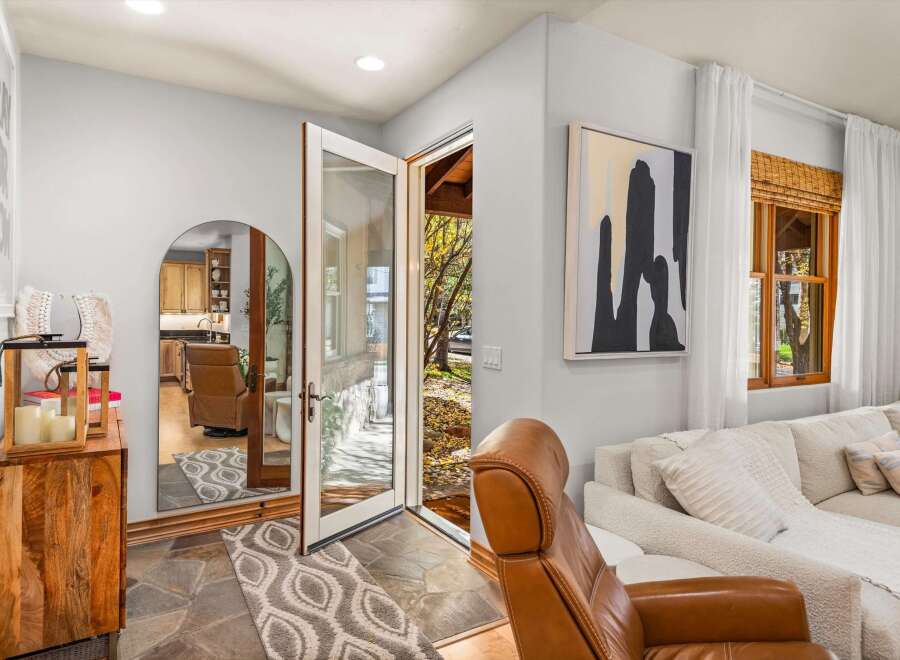 Step into a welcoming entryway featuring a large arched mirror reflecting a cozy kitchen and a plush leather armchair.