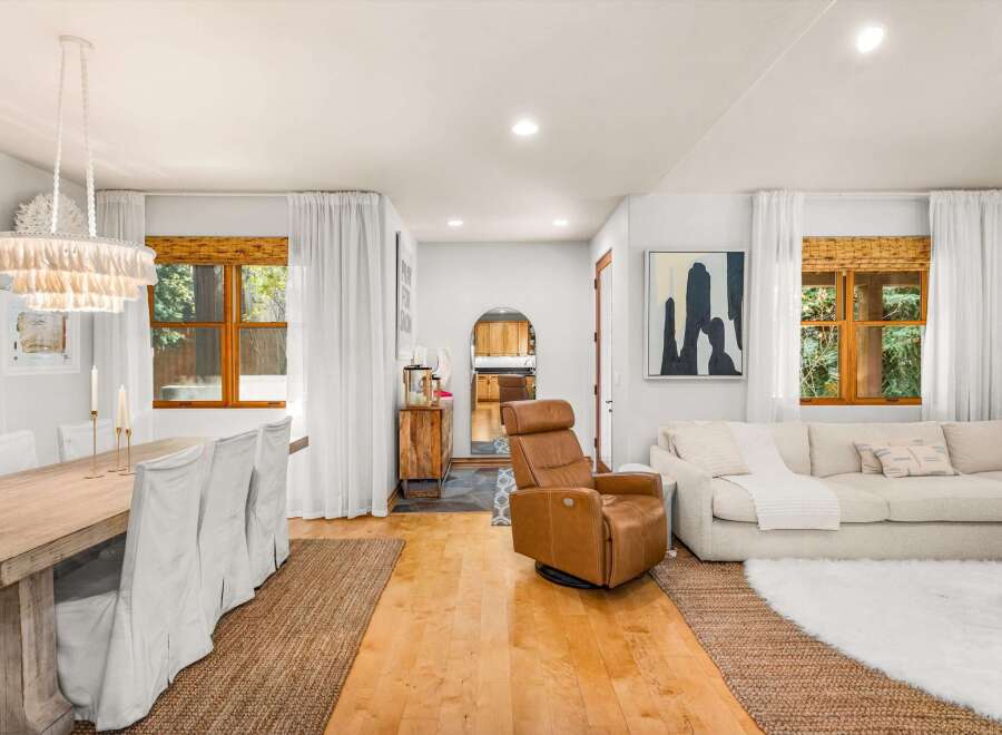 This inviting living and dining area features a rustic wooden dining table with slipcovered chairs, complemented by a stylish tiered chandelier.