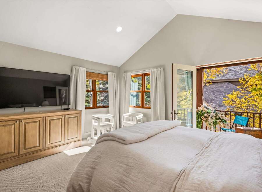 Experience ultimate comfort in this master bedroom, featuring a large flat-screen TV mounted above a charming wooden media console.