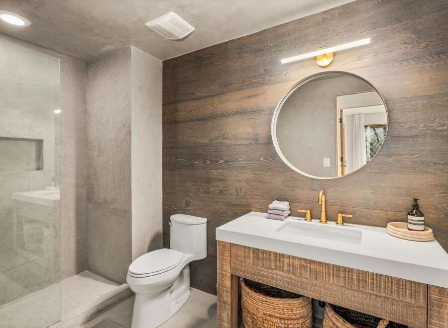 This modern bathroom features a sleek white vanity with a gold faucet, complemented by a rustic wood-paneled accent wall.