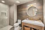 This modern bathroom features a sleek white vanity with a gold faucet, complemented by a rustic wood-paneled accent wall.