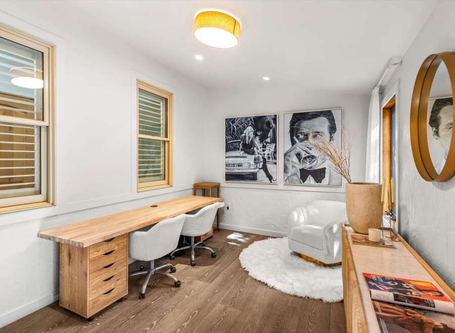 This stylish home office features a long, natural wood desk with ample storage, complemented by two plush, rolling chairs.