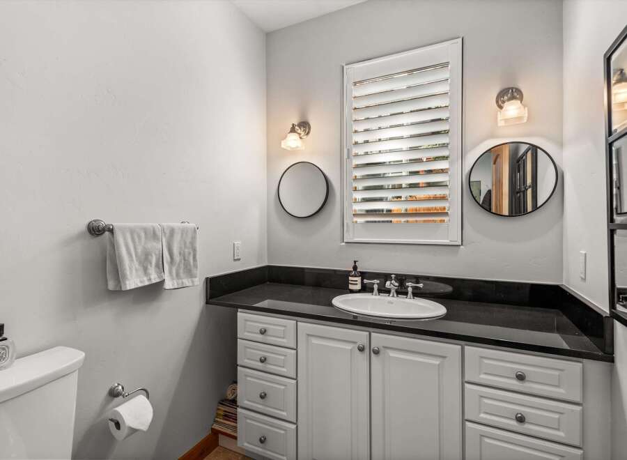 This bathroom features a sleek vanity with a black granite countertop and a white undermount sink, complemented by white cabinetry and drawers.