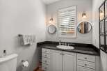 This bathroom features a sleek vanity with a black granite countertop and a white undermount sink, complemented by white cabinetry and drawers.