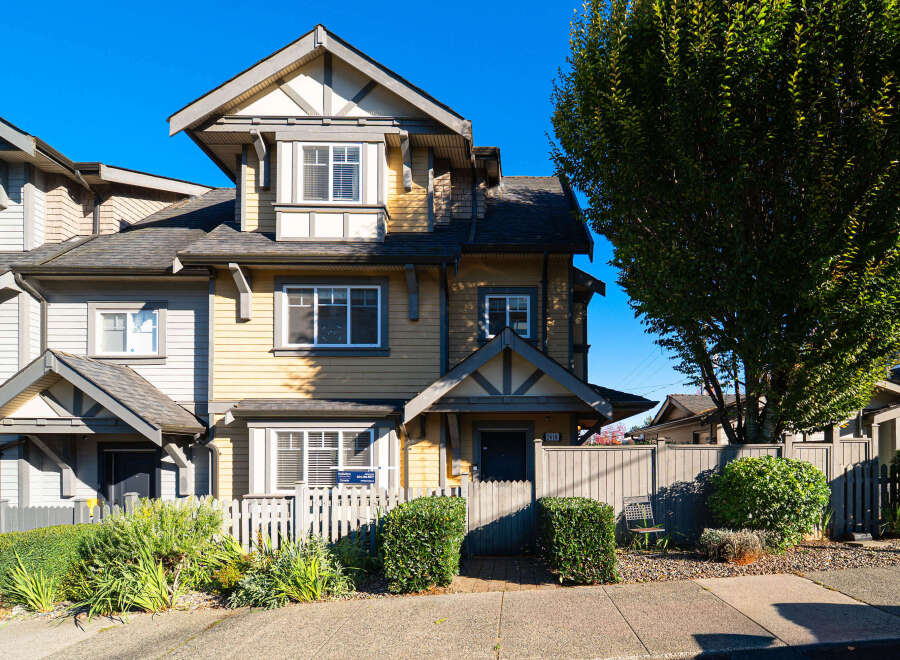 Charming townhouse featuring a classic yellow siding exterior with contrasting grey trim and a dark shingled roof.