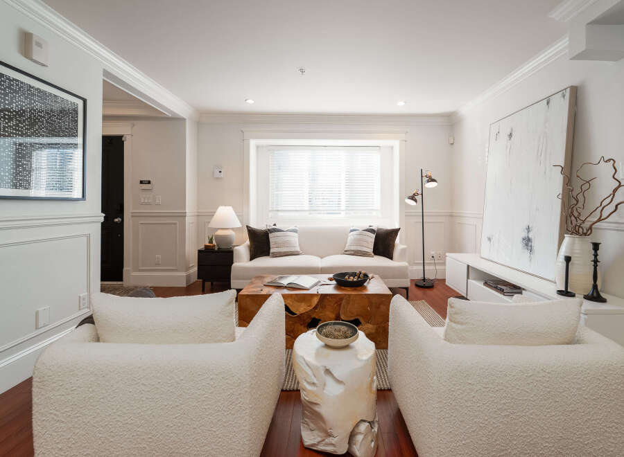 Step into this inviting living room, featuring a plush white sofa adorned with decorative pillows, perfectly complemented by two cozy boucle armchairs.