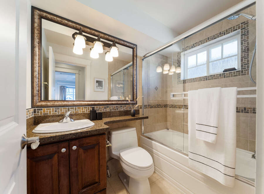 This beautifully appointed bathroom features a spacious vanity with a granite countertop and a dark wood cabinet, complemented by a large, ornate mirror with a vanity light fixture above.