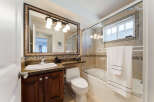 This beautifully appointed bathroom features a spacious vanity with a granite countertop and a dark wood cabinet, complemented by a large, ornate mirror with a vanity light fixture above.