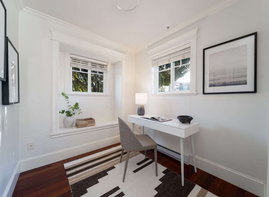 This bright and airy home office features a sleek white desk with a modern lamp and decorative bowl, complemented by a comfortable grey chair.