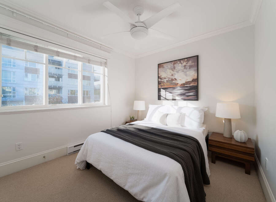 This cozy bedroom features a comfortable queen-size bed dressed in crisp white linens and a dark gray throw blanket.