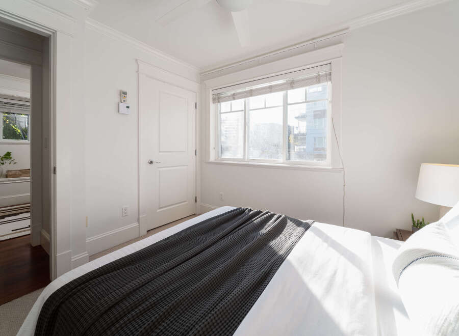 Step into this bright and airy bedroom, featuring a comfortable bed adorned with a stylish dark grey throw blanket.