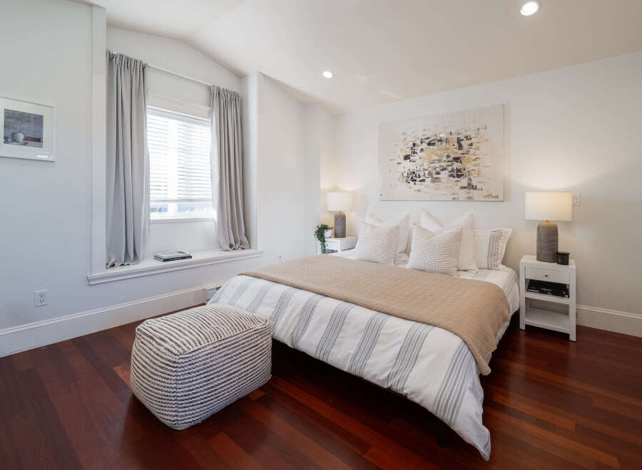 Experience serene comfort in this beautifully appointed bedroom, featuring a plush queen-size bed dressed in crisp white linens with subtle grey stripes.