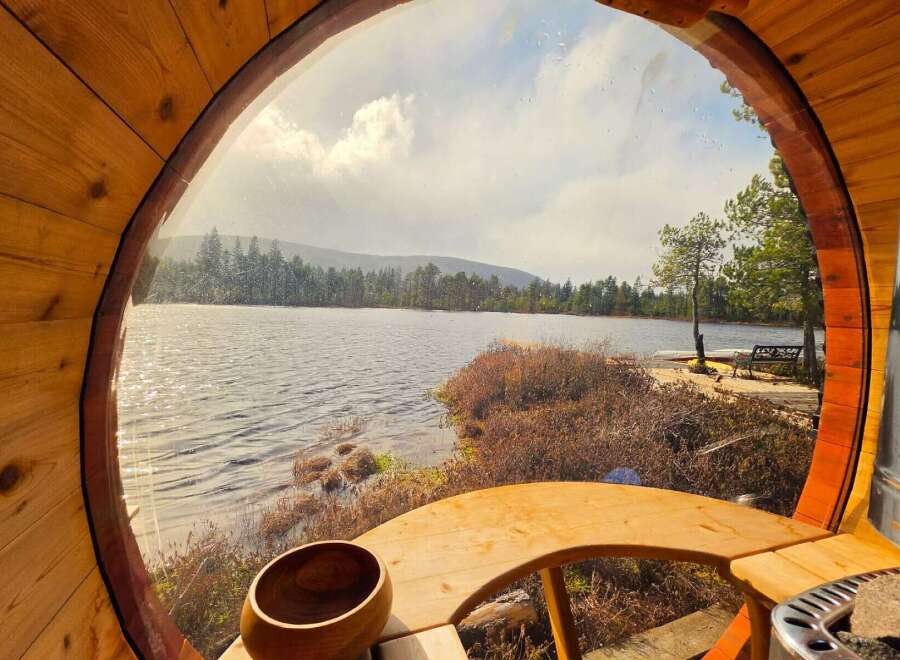 Experience serene lakeside living from this unique barrel sauna, offering breathtaking views of the tranquil water and surrounding pine forest.