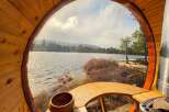 Experience serene lakeside living from this unique barrel sauna, offering breathtaking views of the tranquil water and surrounding pine forest.