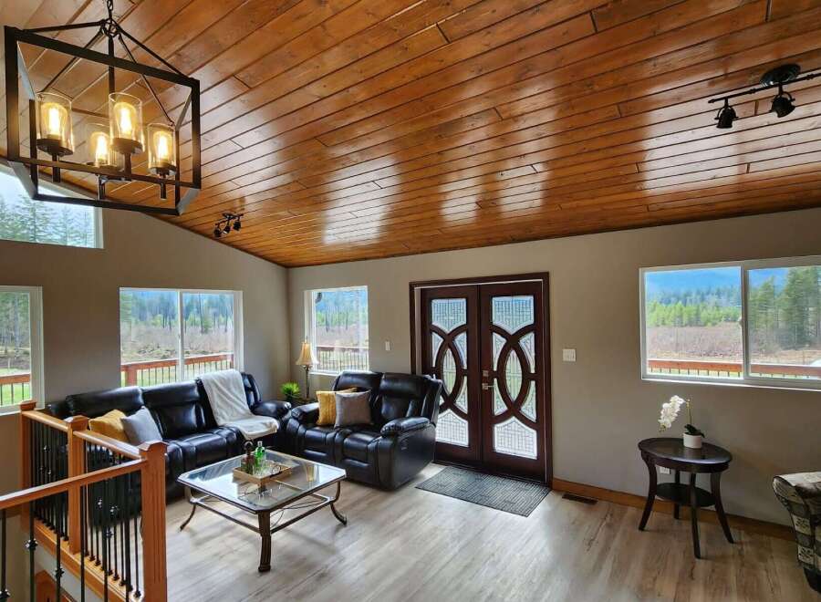 Experience breathtaking mountain views from this stunning living room, featuring a warm, wood-paneled ceiling and a modern black chandelier.