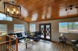 Experience breathtaking mountain views from this stunning living room, featuring a warm, wood-paneled ceiling and a modern black chandelier.