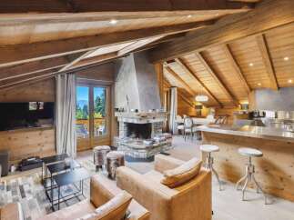 Experience luxurious mountain living in this stunning chalet, featuring a grand stone fireplace and a modern open-plan kitchen with a sleek stainless steel island.