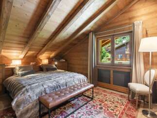 Experience rustic charm in this attic bedroom, featuring exposed wooden beams and walls that create a warm, inviting ambiance.