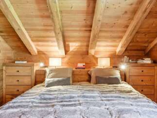 Experience rustic charm and cozy comfort in this beautifully appointed bedroom, featuring exposed wooden beams and warm wood paneling.