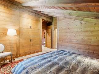 Experience rustic luxury in this charming bedroom, featuring warm wooden walls and a vaulted ceiling with exposed beams.