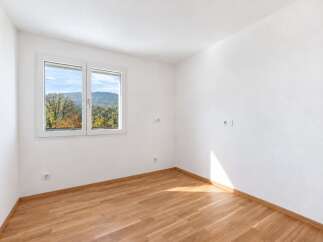 This empty room features a large window with a scenic view of autumn foliage and rolling hills.