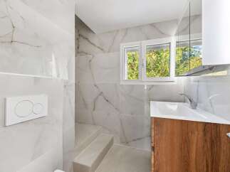 This modern bathroom features elegant white marble-look tiles on the walls and a sleek wooden vanity with a white sink.