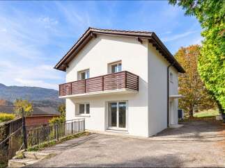 Discover this charming white house with a modern wooden balcony, perfect for enjoying the scenic mountain views.