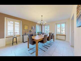 This elegant dining room features a large wooden table surrounded by comfortable upholstered chairs, perfect for hosting family and friends.