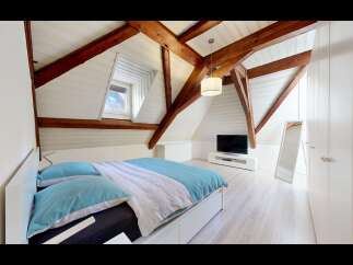 Discover this charming attic bedroom featuring exposed wooden beams and a sloped ceiling, creating a cozy and rustic ambiance.
