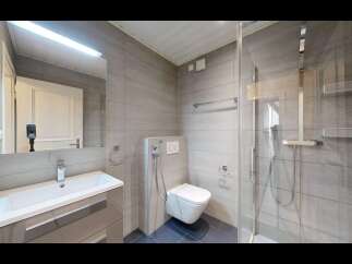 This modern bathroom features a sleek vanity with a white basin and chrome faucet, complemented by a large mirror with an integrated light.