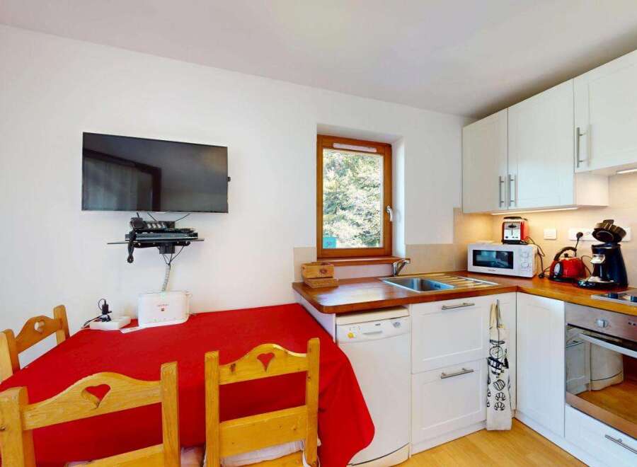 This charming kitchen features a cozy dining area with a red tablecloth and wooden chairs, perfect for intimate meals.