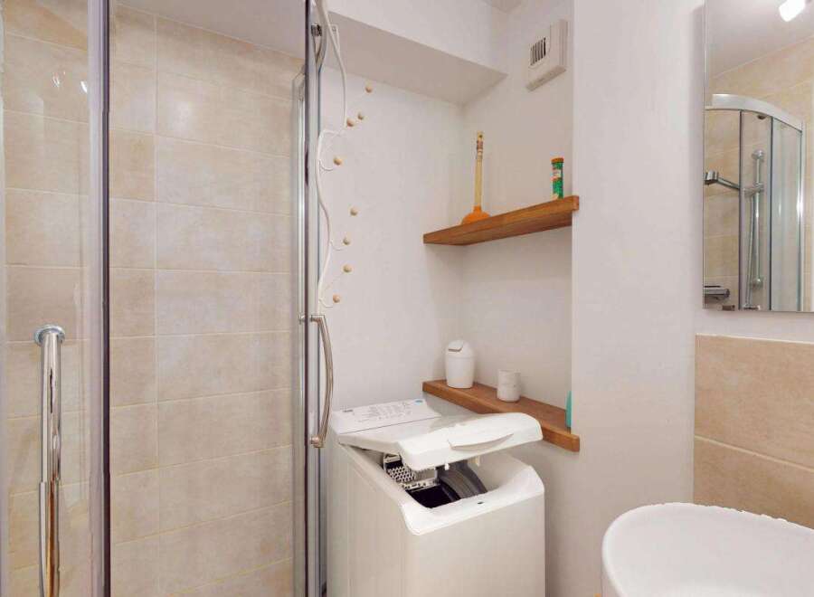 This modern bathroom features a convenient washing machine next to a sleek glass-enclosed shower.