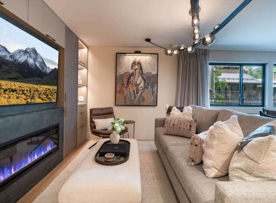 Experience luxury living in this stunning living room, featuring a modern fireplace with vibrant blue flames and a large flat-screen TV displaying a majestic mountain landscape.