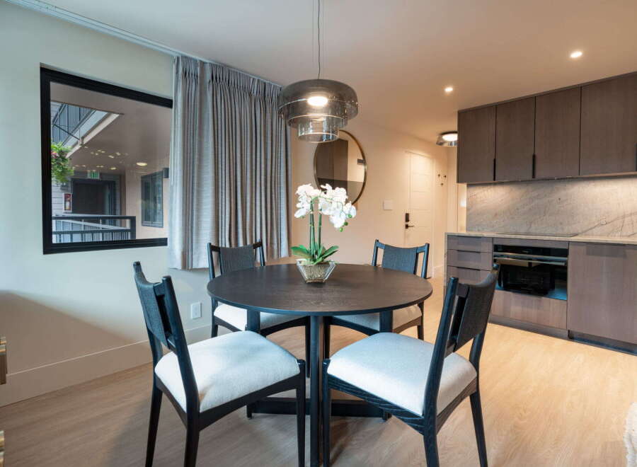 This modern dining area features a sleek, dark wood round table surrounded by four upholstered chairs with black frames.
