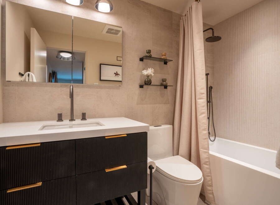 This modern bathroom features a sleek vanity with fluted drawers and gold hardware, complemented by a minimalist white countertop and sink.