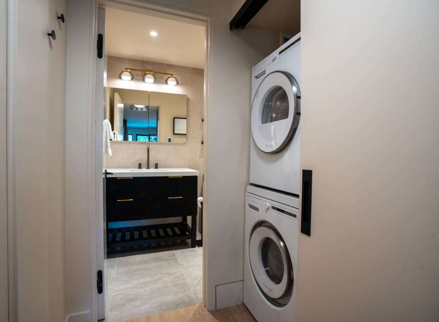 This modern bathroom features a sleek black vanity with gold hardware, complemented by a large mirror and stylish vanity lighting.
