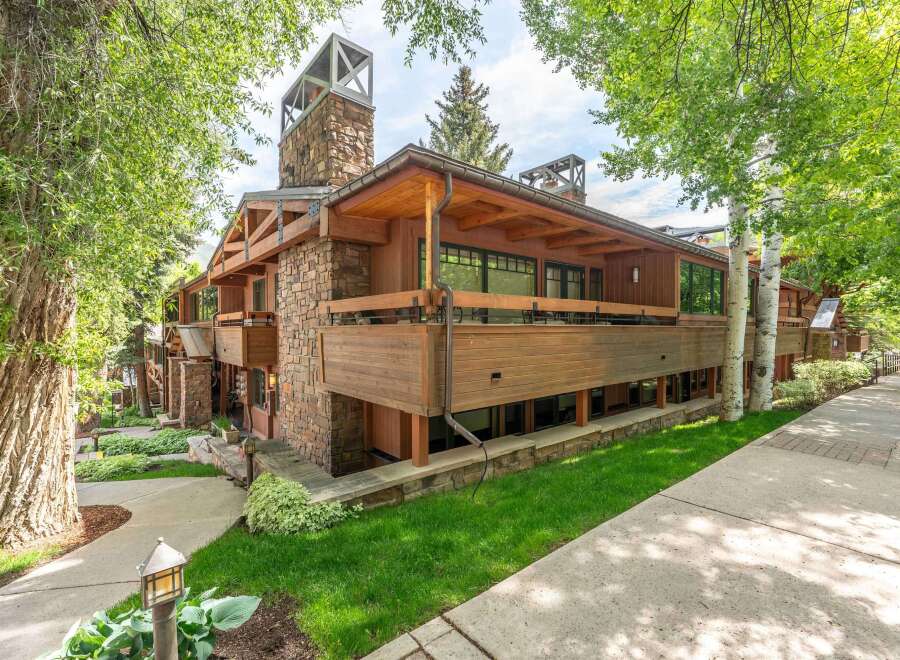 This stunning mountain home features a striking stone chimney with a modern metal cap, complemented by warm wooden siding and exposed beams.