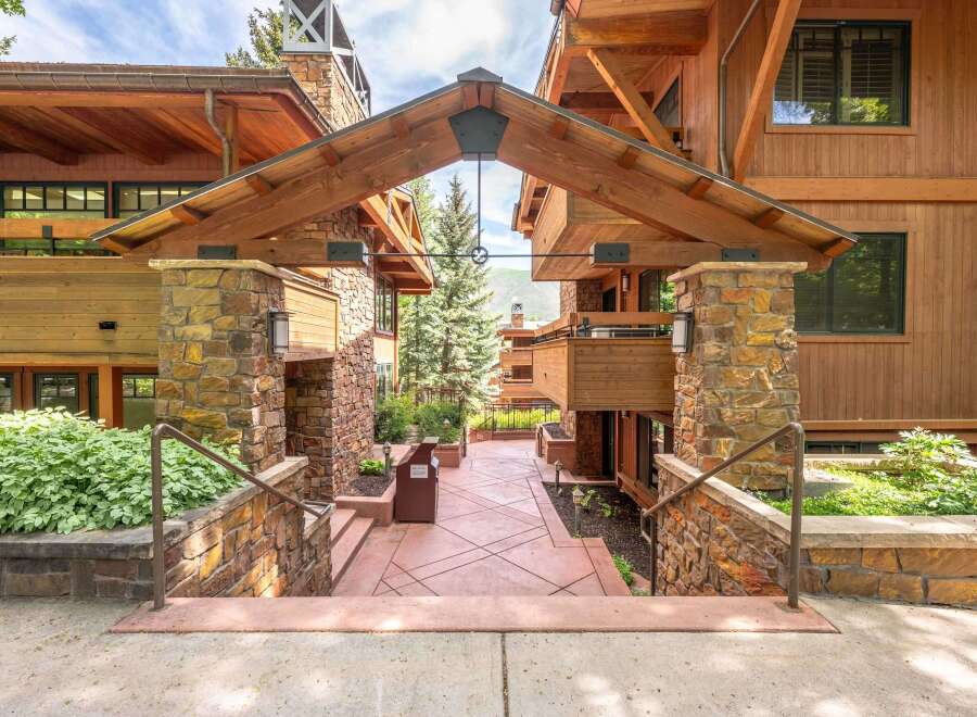 Experience the charm of this mountain-style property, featuring a grand entrance with a covered walkway supported by stone pillars and exposed wooden beams.