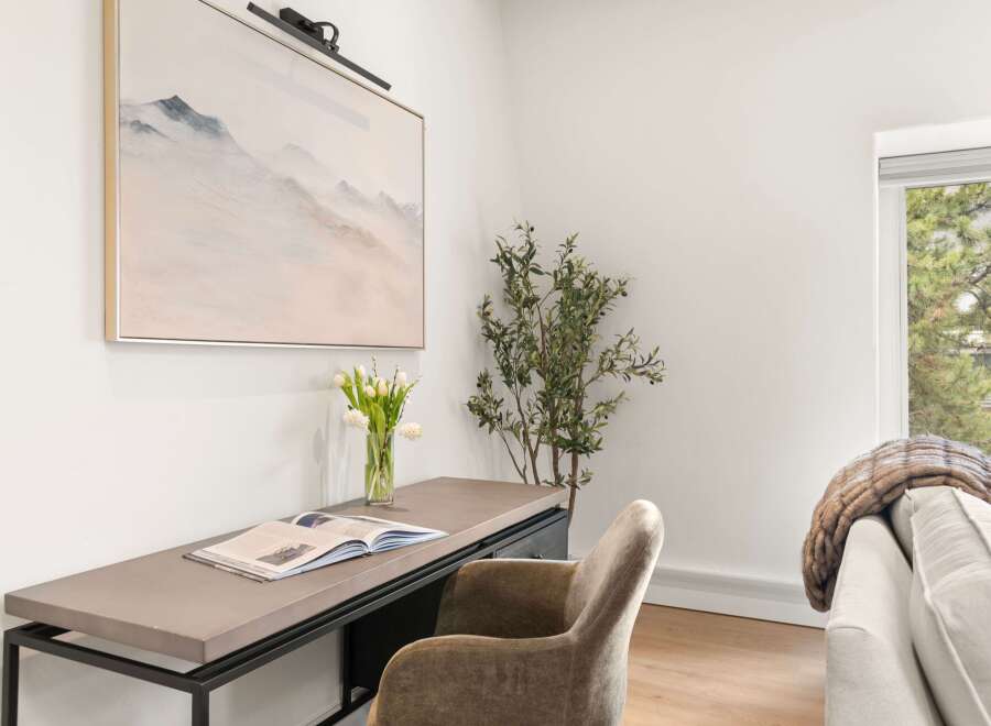 This elegant home office features a sleek desk with an open book and a vase of tulips, complemented by a plush velvet chair.