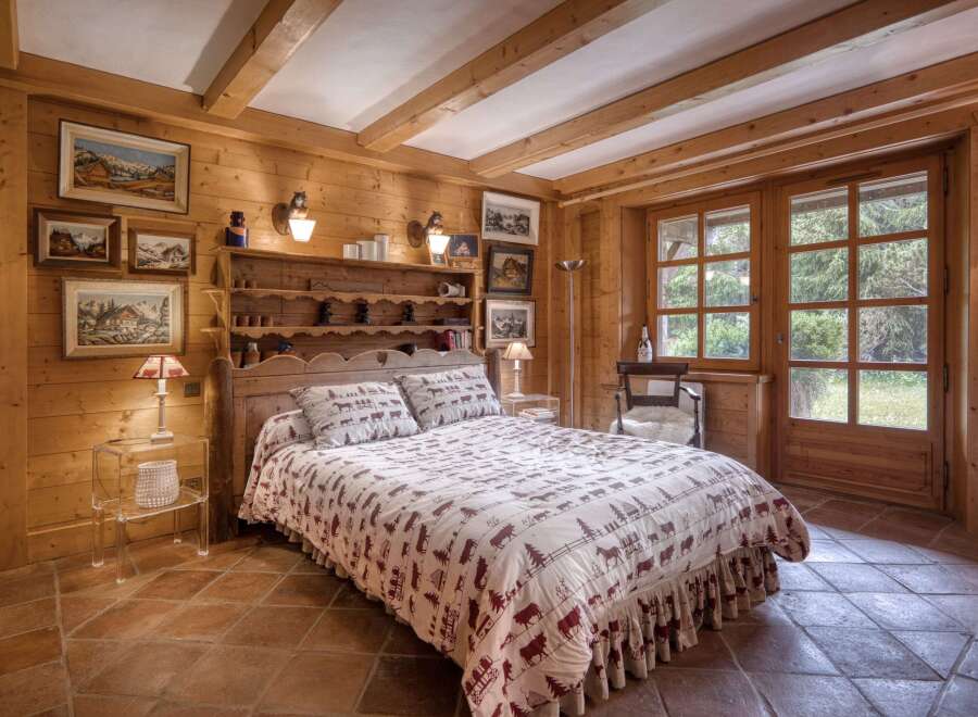 Experience rustic charm in this beautifully appointed bedroom, featuring warm wooden walls and exposed beams.
