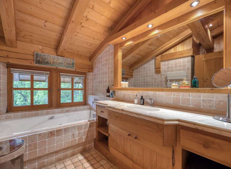 Experience rustic charm in this bathroom featuring a deep soaking tub with a view of lush greenery through the wooden-framed windows.