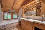 Experience rustic charm in this bathroom featuring a deep soaking tub with a view of lush greenery through the wooden-framed windows.