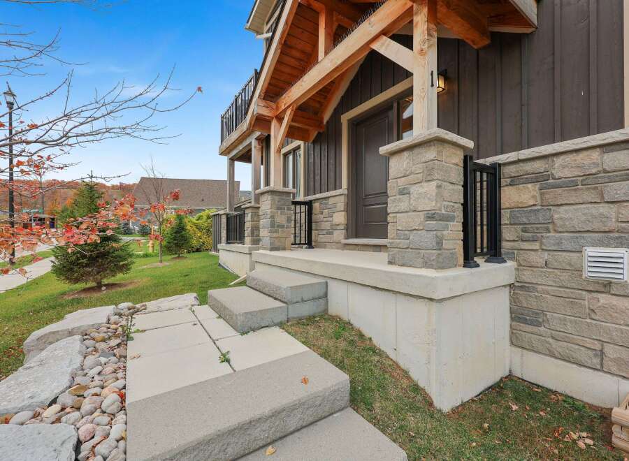 Experience modern living in this stunning home featuring a striking facade with stone accents and a covered porch with exposed wooden beams.