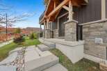 Experience modern living in this stunning home featuring a striking facade with stone accents and a covered porch with exposed wooden beams.