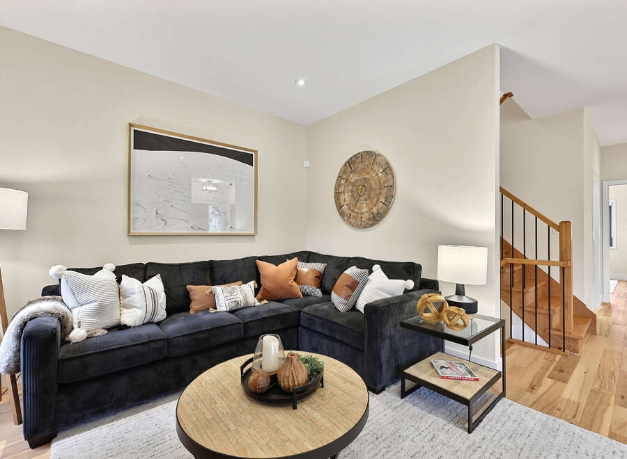 Step into this inviting living room, featuring a plush, dark sectional sofa adorned with a variety of decorative pillows and a cozy throw blanket.