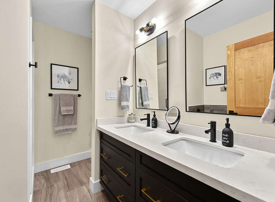 This modern bathroom features a sleek double vanity with dark wood cabinetry and elegant gold hardware.