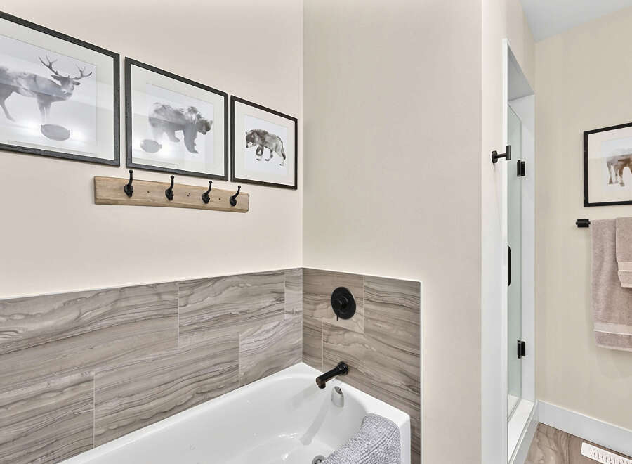This modern bathroom features a sleek bathtub with marble-patterned tile accents and black fixtures.