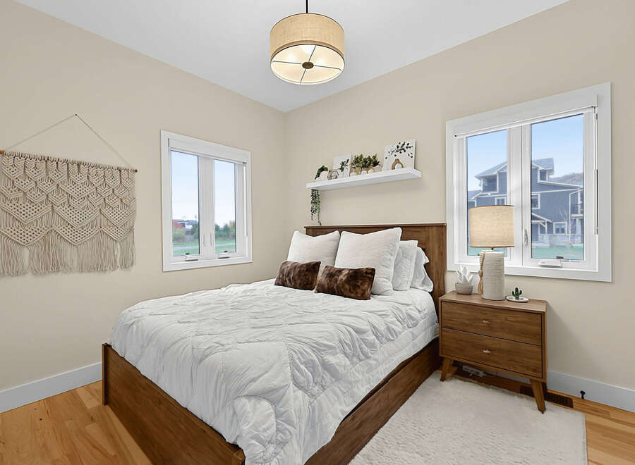 This charming bedroom features a cozy queen-size bed with a plush white comforter and decorative pillows, complemented by a warm wooden bed frame.