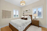 This charming bedroom features a cozy queen-size bed with a plush white comforter and decorative pillows, complemented by a warm wooden bed frame.