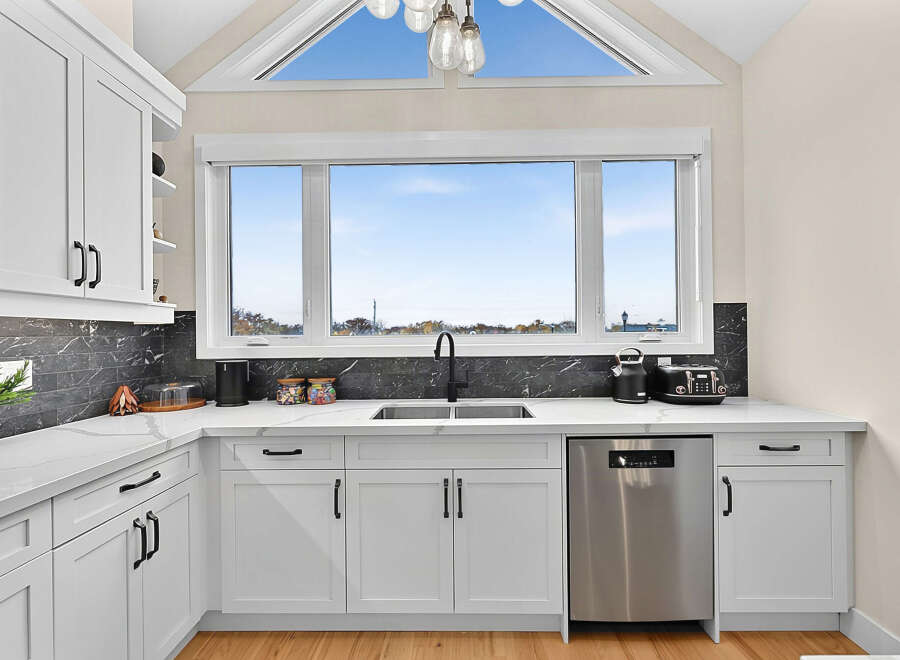 Experience modern living in this stunning kitchen featuring sleek white cabinetry with black hardware, complemented by a striking dark marble backsplash.